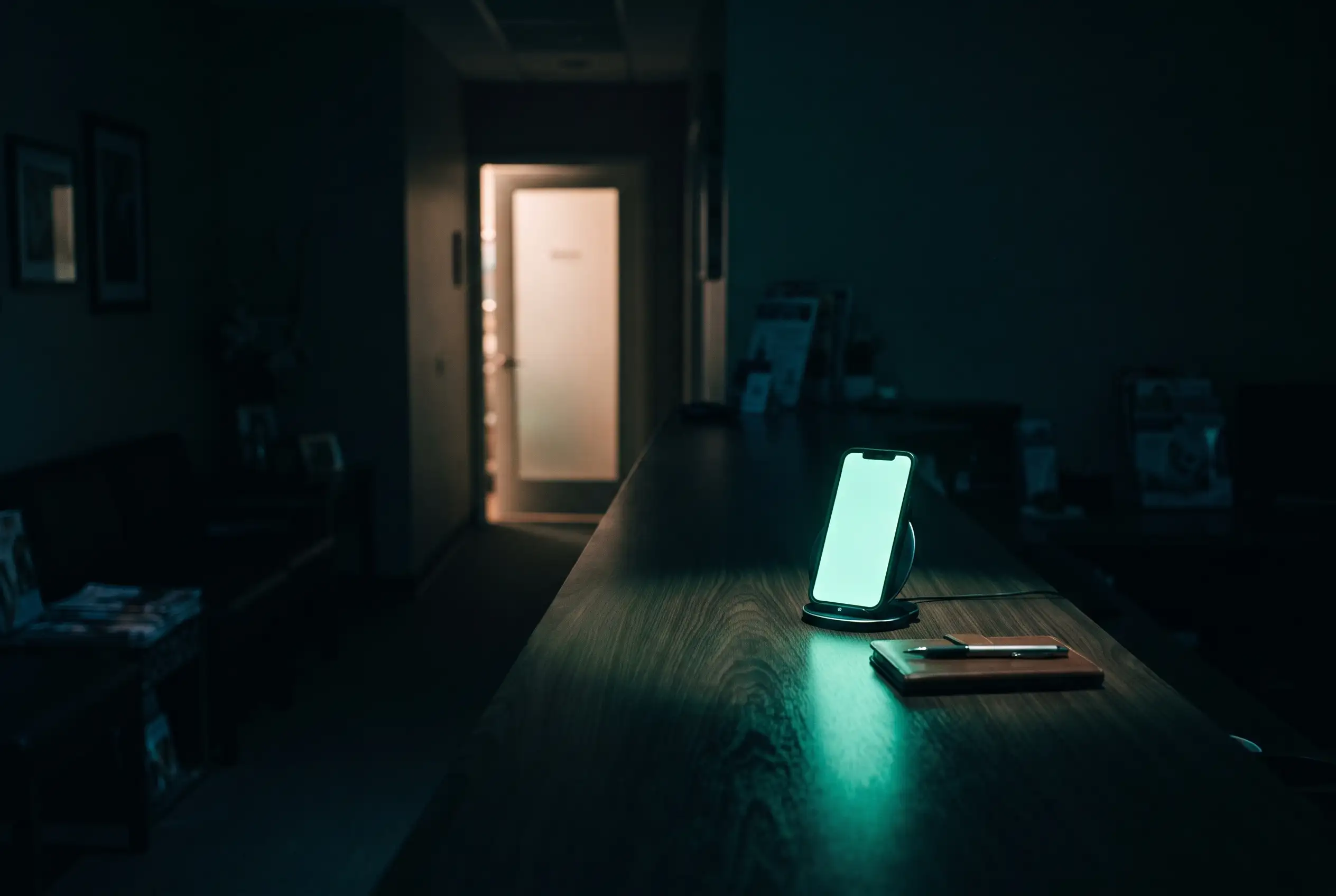 A dental practice reception after hours, the front desk in shadow, a phone glowing on the desk.